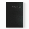 A black textured notebook with the words 'feeling and ugly' printed in white serif font near the top, shown against a plain white background.